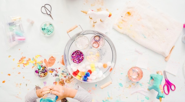 Photo step by step. little girls decorating paper mache unicorn with glitter and paper flowers.