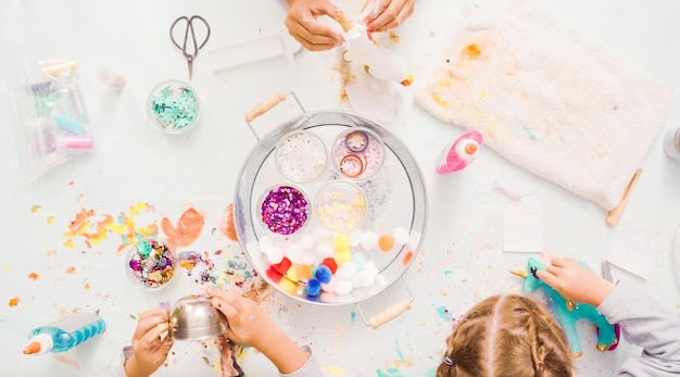 Step by step. Little girls decorating paper mache unicorn with glitter and paper flowers.