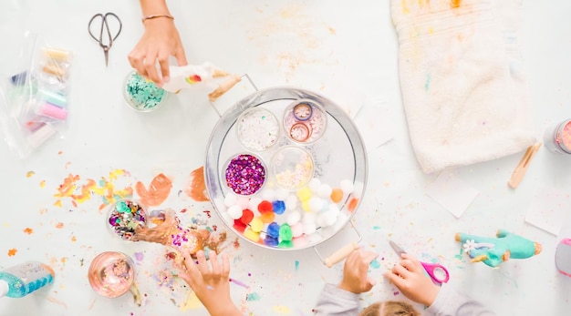 Step by step. Little girls decorating paper mache unicorn with glitter and paper flowers.