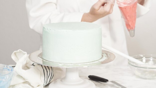 Photo step by step. piping buttercream rosettes on top of round three-layer vanilla cake.