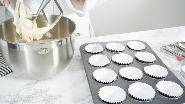 Photo step by step. scooping batter with batter scooper into cupcake pan lined with paper cupcake liners.