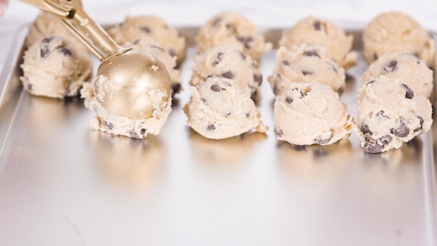 Step by step. Scooping homemade chocolate chip cookies with metal dough scoop to the baking sheet.