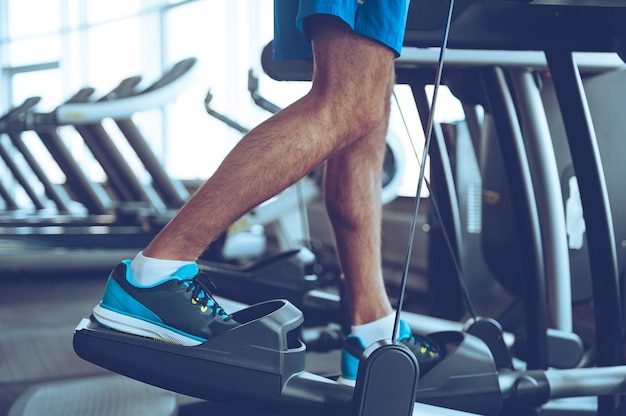 Step by step. Side view part of young man in sports shoes working out on stepper at gym