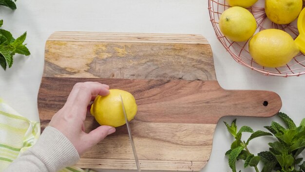 Step by step. Slicing organic lemon on wood cutting board.