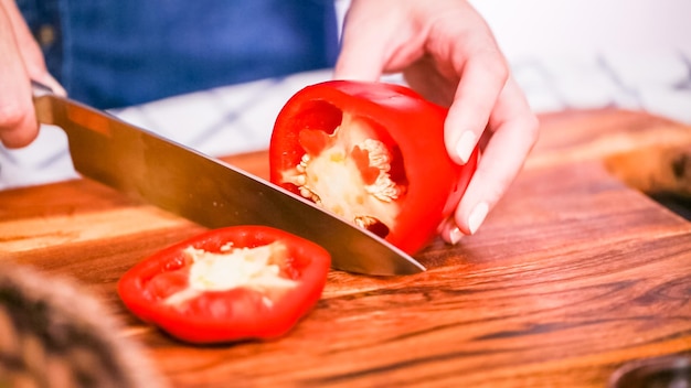 Step by step. Slicing red bell pepper on a wood cutting board.