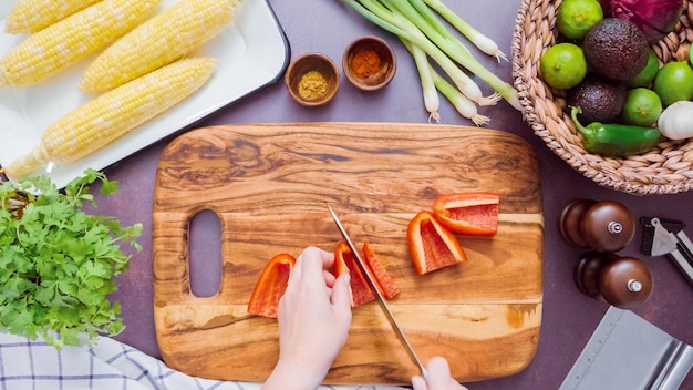 Step by step. Slicing red bell pepper on a wood cutting board.