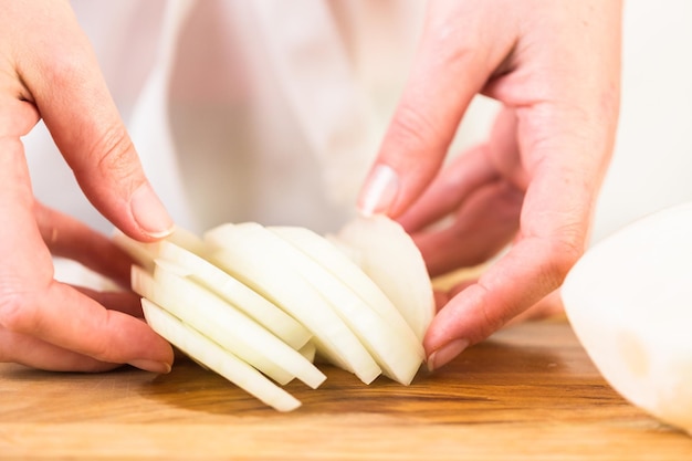 Step by step. Slicing yellow onion with kitchen knife on a cutting board.