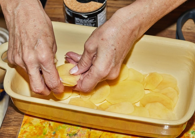 Stepbystep recipe of potato gratin Hands stack potato slices to glass baking dish Potato casserole