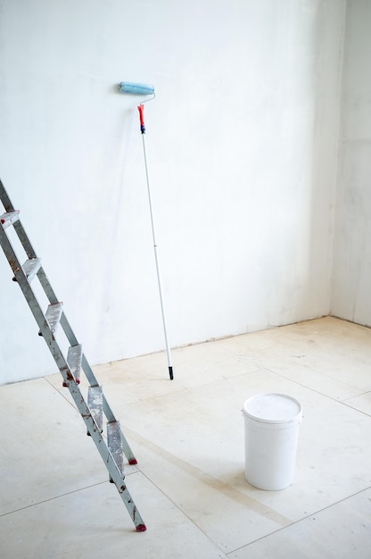 Foto scala un secchio di plastica chiuso di vernice e un rullo di vernice nella stanza. preparazione per la riparazione