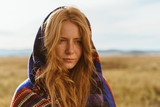 In the steppe stands a girl in an ethno cape with long loose hair without makeup with natural beauty