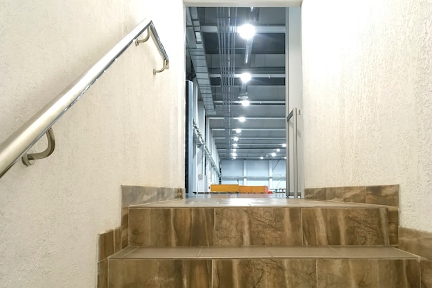 Steps stairs from tiles next to plastered wall into open door,\
in industrial modern building. staircase with handrails in\
industrial style. copy space. close-up. indoors.