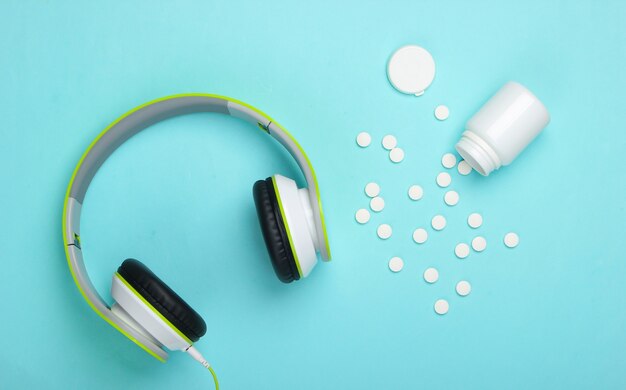 Stereo headphones and pills on a blue surface