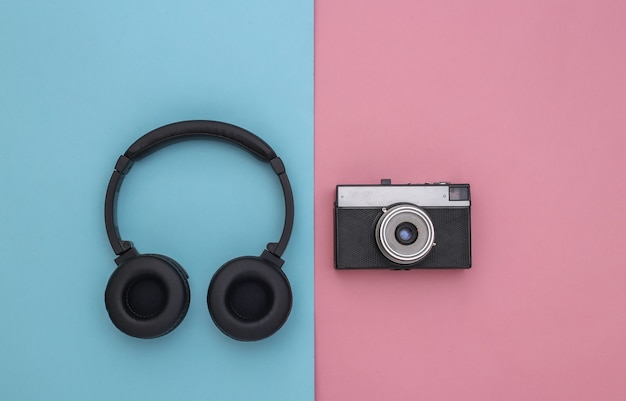 Stereo headphones and retro camera on blue-pink pastel background. Top view