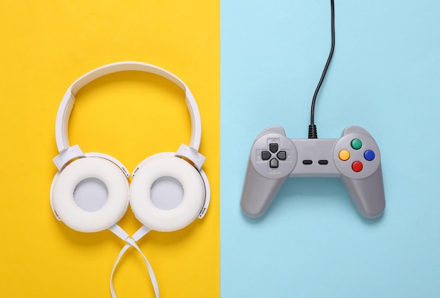 Stereo headphones and retro gamepad on a blueyellow background Gaming layout Top view