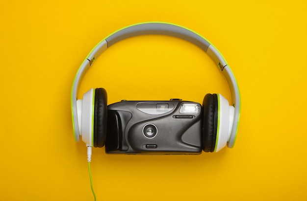 Stereo headphones with a retro film camera on yellow surface