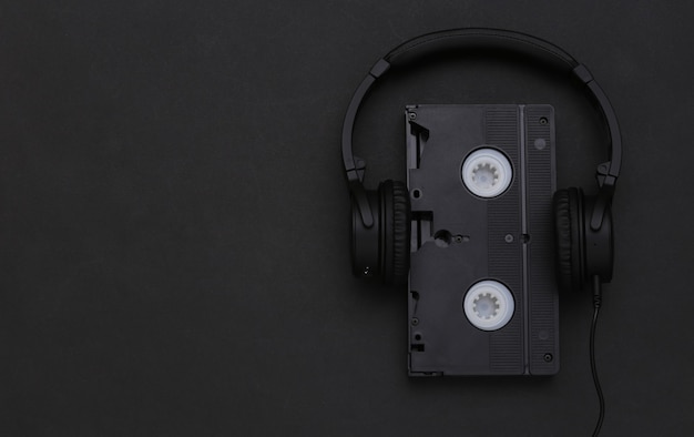 Stereohoofdtelefoons met videocassette op zwarte achtergrond. Bovenaanzicht