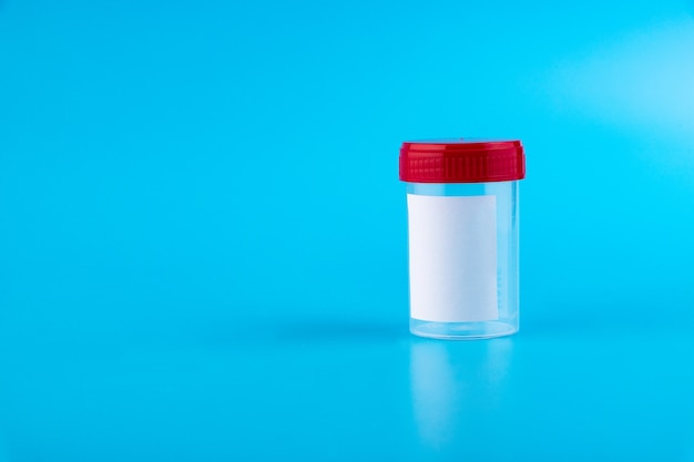 Sterile transparent blank plastic container for analysis. red\
lid. sterile medical container for biomaterial. isolated on a blue\
background.