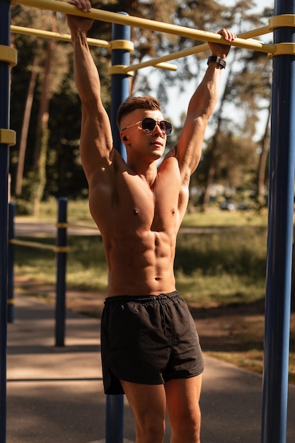 Sterk sportmanmodel met zonnebril en draadloze koptelefoon oefenen en trainen in het park Atletische man met gespierde torso