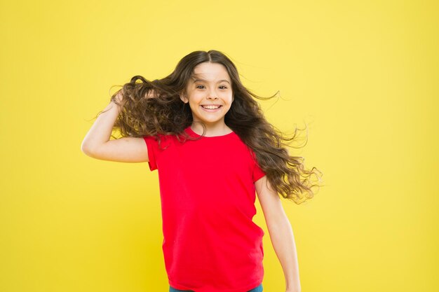 Sterke, aanhoudende winden kunnen klitten en haken en ogen veroorzaken in golvend en krullend lang haar. Dingen die je doet om je haar te beschadigen. Meisje schattig kind lang golvend haar gele achtergrond. Wind kan ook het haar beschadigen.