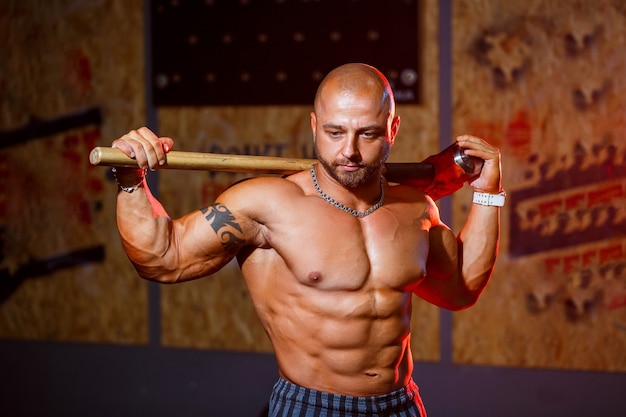 Sterke atletische man poseren met een sporthamer op de achtergrond van de sportschool. Een sterke bodybuilder met perfecte buikspieren, schouders, biceps, triceps en borst.