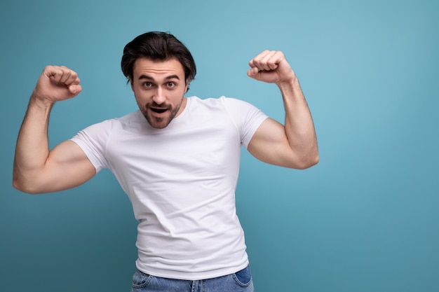 Sterke brunette jonge man in witte t-shirt met biceps op studio achtergrond met copyspace