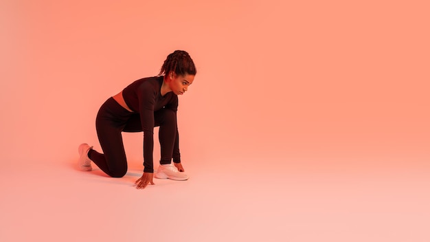 Sterke en fitte sportieve zwarte runner-vrouw die hurkt, begint naar vrije ruimte over rood neon te kijken