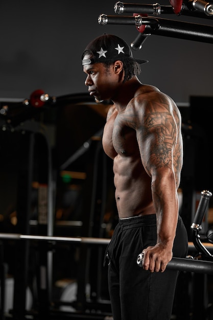 Sterke en gespierde donkere huid man traint op moderne apparatuur in de sportschool Portret van gespierde opgepompte fitnesstrainer