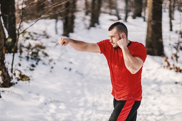 Sterke gespierde sportman sparring in de natuur op besneeuwde winterdag. Winterfitness, sparren, sporten