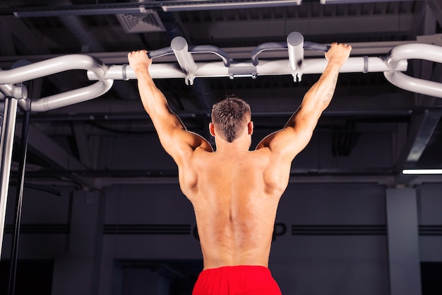 Sterke jonge man doet pull-up oefening op horizontale balk in de sportschool. sport, fitness, gymnastiektraining.