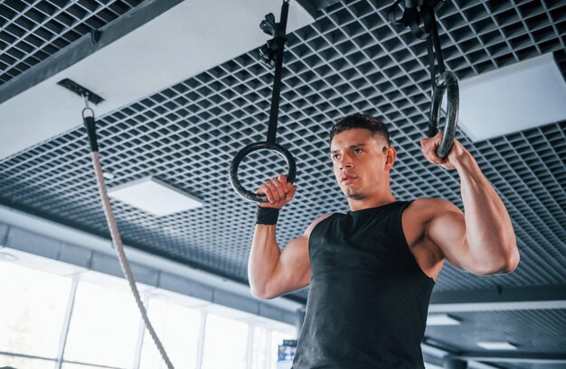 Sterke jonge man in sportieve kleding die oefeningen doet op gymnastiekringen in de sportschool