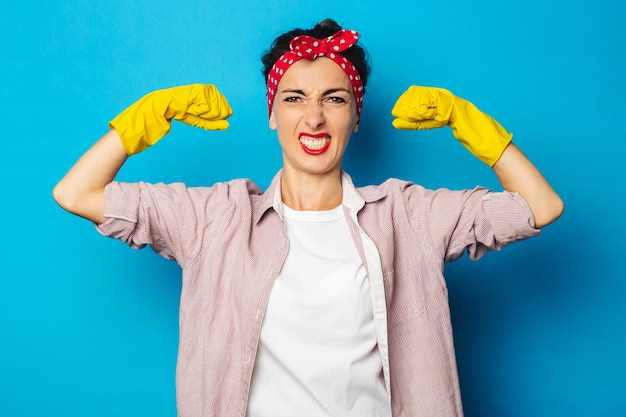 Sterke jonge vrouw die biceps toont in het schoonmaken van handschoenen op blauwe oppervlakte