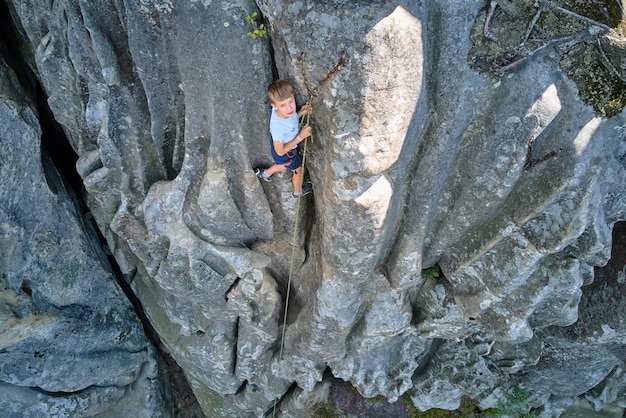 Sterke kindklimmer die steile muur van rotsachtige berg beklimt Jonge jongen die moeilijke route overwint Bezig zijn met extreme sporten hobbyconcept