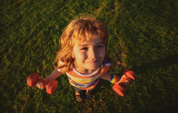 Sterke kleine jongen grappig gezicht van schattig kind met halters kinderen sport gezondheidsconcept