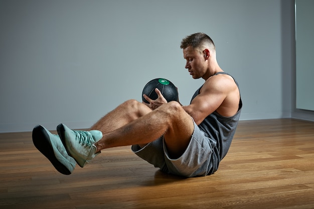 Sterke man doen oefening met med bal. Foto van de mens perfecte lichaamsbouw op grijze muur. Kracht en motivatie.