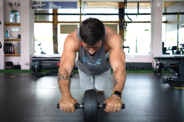 Foto sterke man doet buikspieren op de vloer met een roller in de sportschool