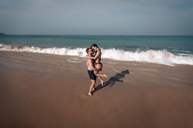 Sterke man houdt zijn vriendin in zijn armen op het prachtige strand aan de blauwe zee, liefde en tederheid.