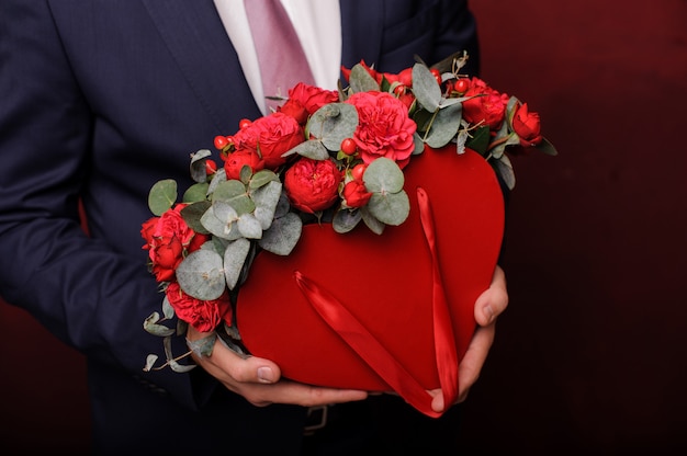 Sterke man in het pak met een rode doos rozen in een hand