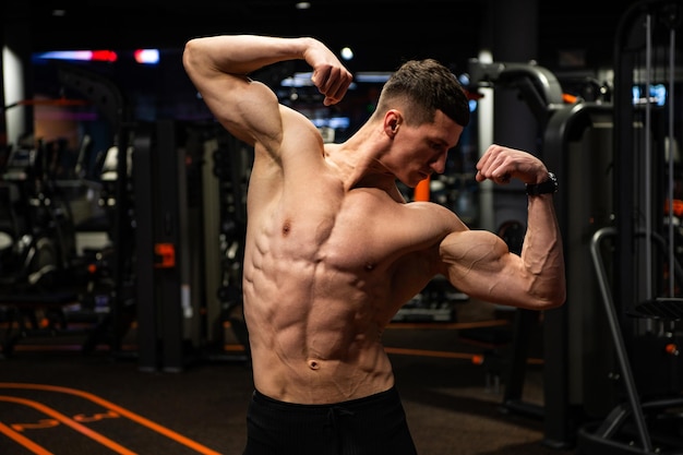 Sterke man met fit torso buigende armen spieren staande in dubbele biceps pose in sportschool, kracht