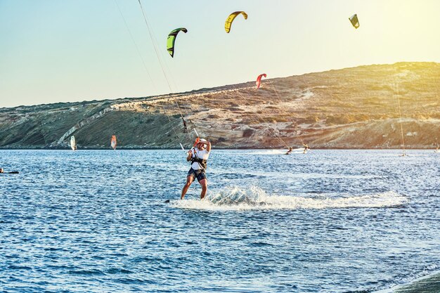 Sterke sporters gaan kitesurfen op azuurblauw zeewater op Prasonisi-strand bij zonsondergang in Griekenland