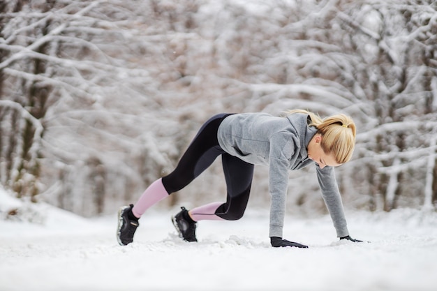 Sterke sportvrouw die opwarmoefeningen doet terwijl ze in de winter in de sneeuw in de natuur staat. Gezonde levensstijl, winterfitness