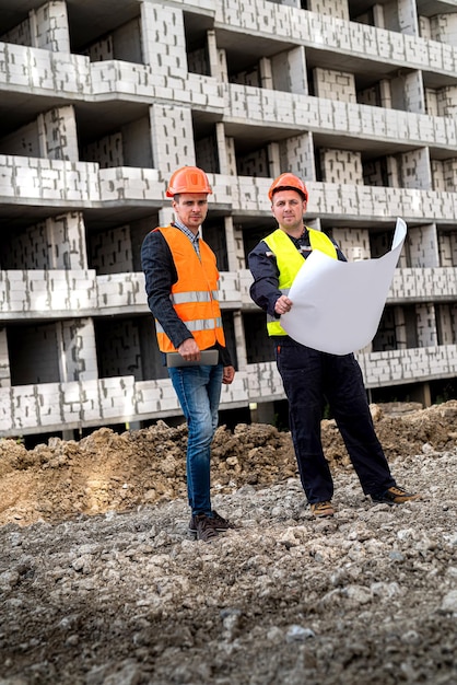 Sterke twee arbeiders in helmuniformen met bouwplan dat zich op de bouw van huizen bevindt Bouwconcept