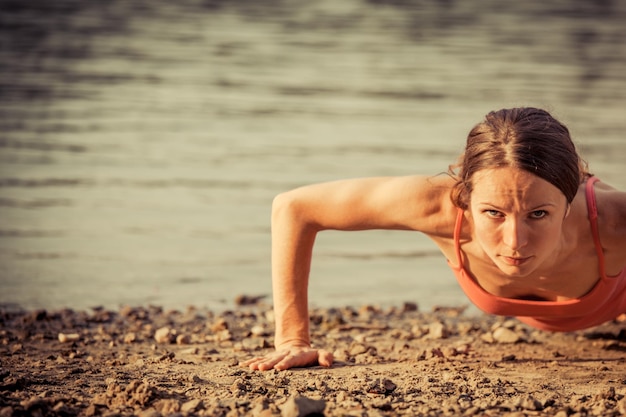 Sterke vrouw doet push-up op het strand Zomersportconcept