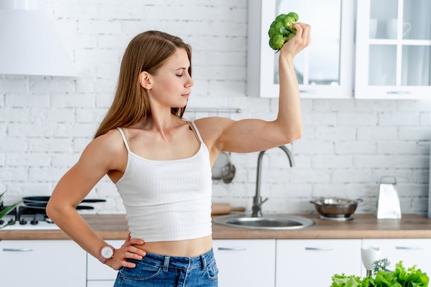 Sterke vrouw met broccoli in de keuken. Het jonge gezonde meisje toont haar sterke handen.