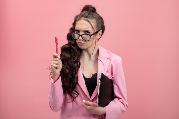 A stern angry demanding woman with glasses elegantly dressed holds a pen and laptop in hand