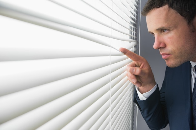 Photo stern attractive businessman spying through roller blind