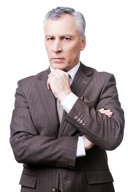 Stern glance of director. thoughtful mature man in formalwear holding hand on chin and looking at camera while standing against white background