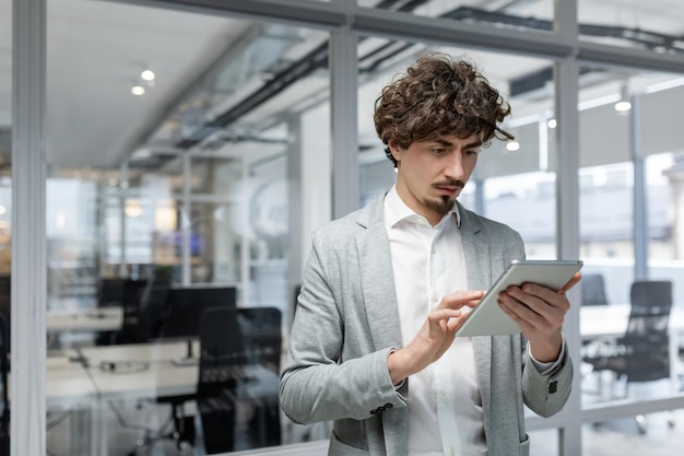 A stern thinking businessman stands inside the office with a tablet computer a man in a business