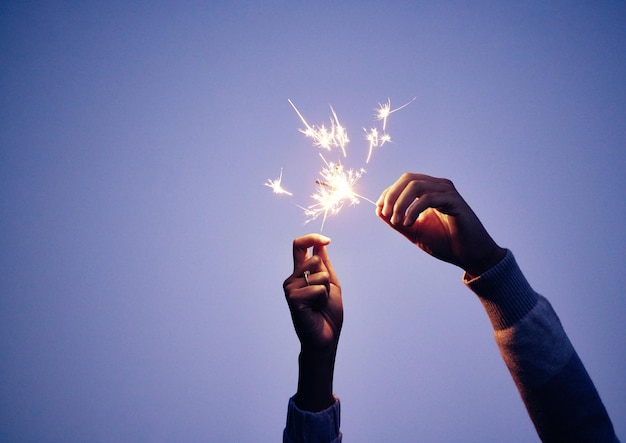 Sterretje hand en persoon 's nachts voor oud en nieuw feest met helder brandend plezier om te vieren Schittering en blauwe nachtelijke achtergrond vieren met vuurwerk of voetzoeker in handen