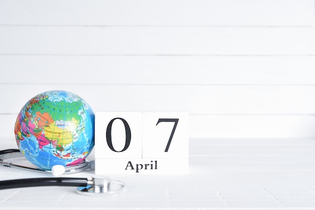 Foto stethoscoop en globe met 7 april tekst houten blok kalender op witte houten achtergrond.