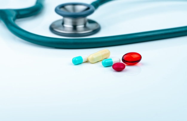 Stethoscoop met blauw-witte capsule, rode zachte gelcapsulepillen en rode ronde tabletten op artsentafel of verpleegsterbureau.
